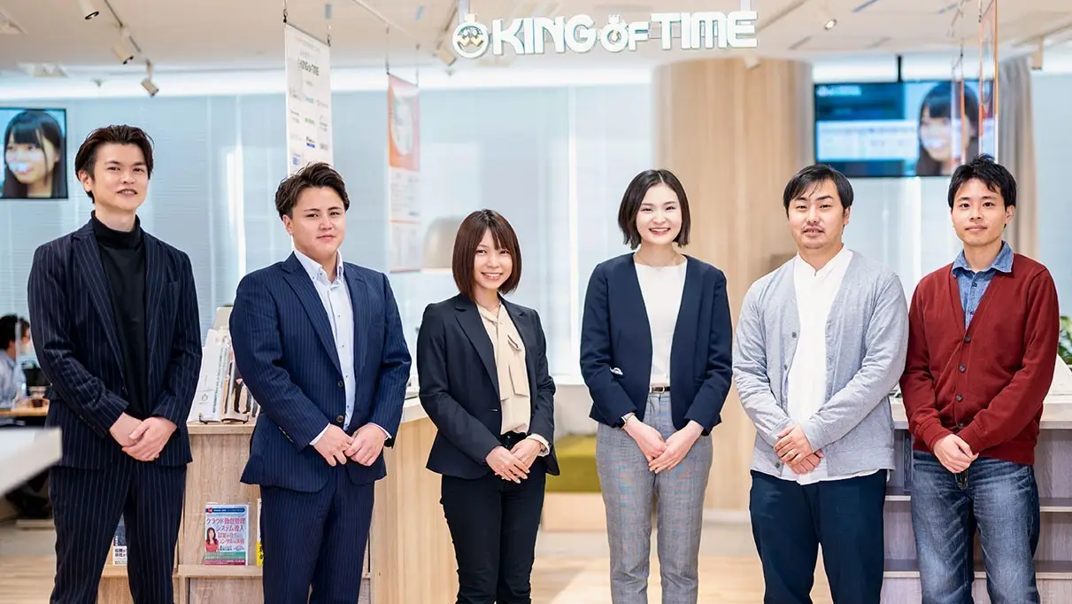 「KING OF TIME」のロゴの下に並んで立っている6人のビジネスパーソンの集合写真の様子。
